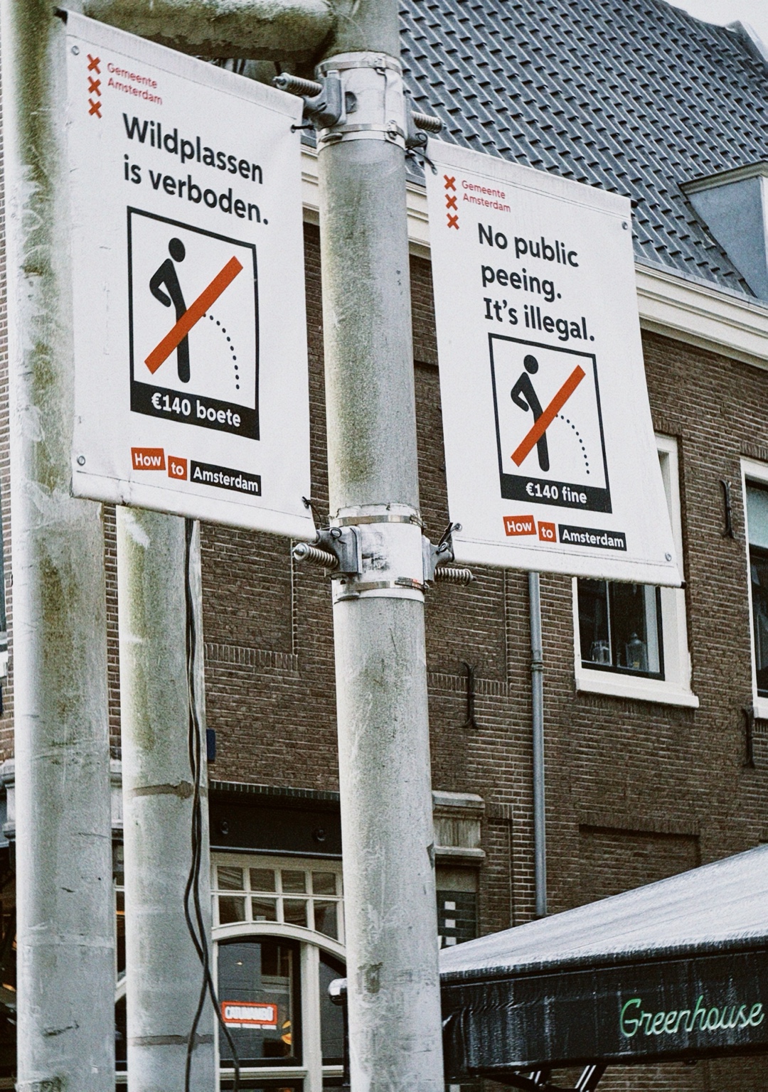 Amsterdam municipal signs warning that public peeing is illegal, with a €140 fine, mounted on a street pole in Amsterdam, Netherlands.