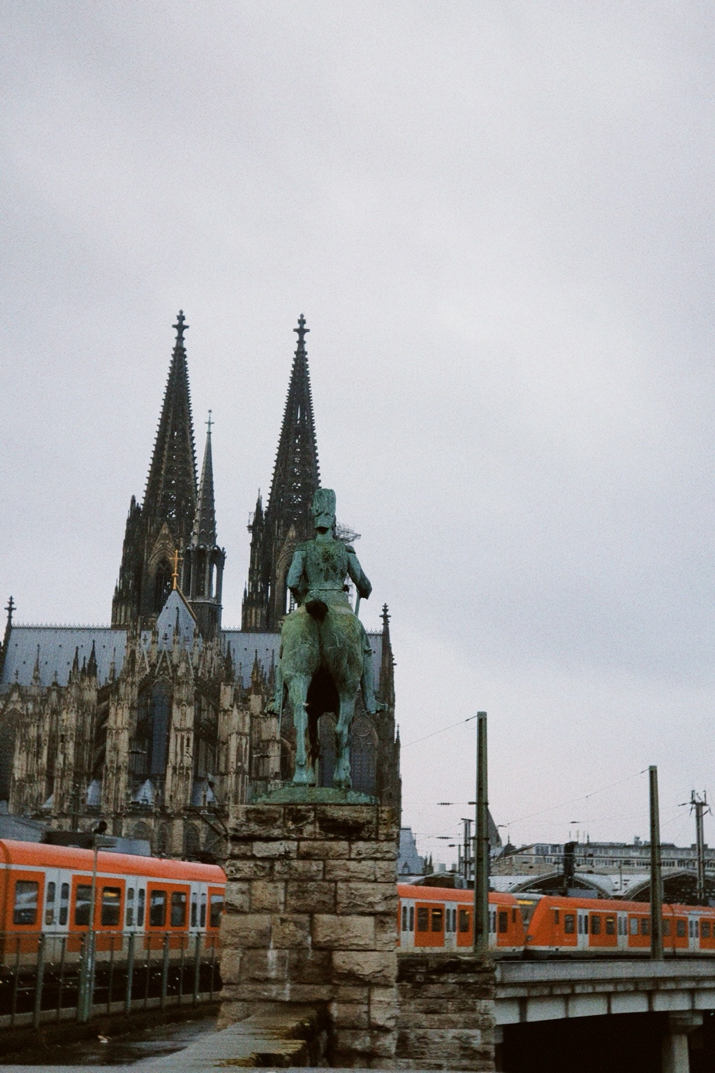Cologne Cathedral behind a bronze equestrian monument with trains in the foreground.