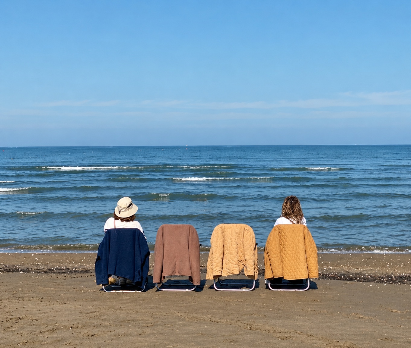 Four deck chairs facing the Caspian Sea in Mazandaran, Iran, with two people seated among the chairs on a sandy beach.