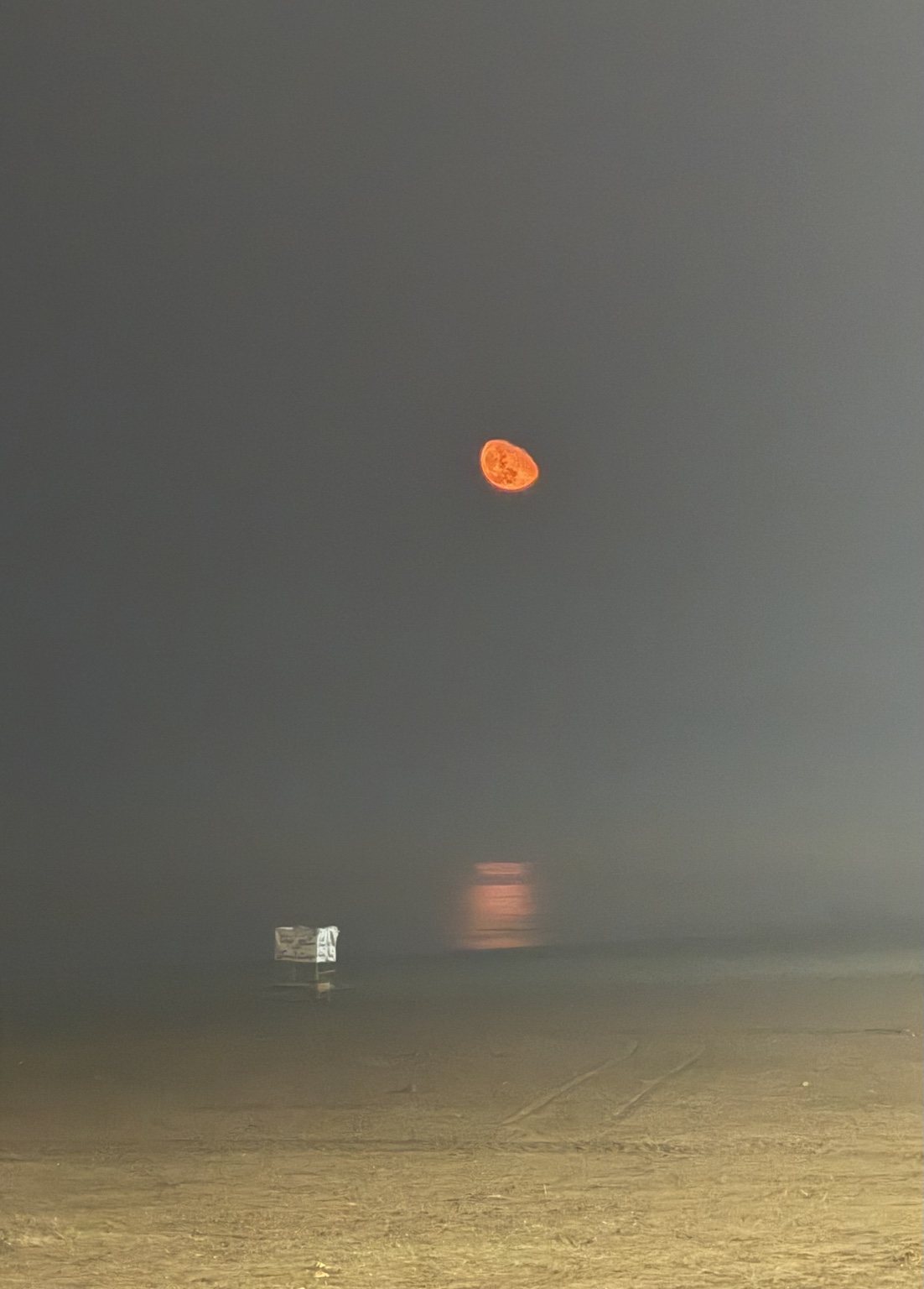 A glowing orange moon above a fog-covered shoreline in Mazandaran, Iran, with its warm reflection diffused across the misty water.