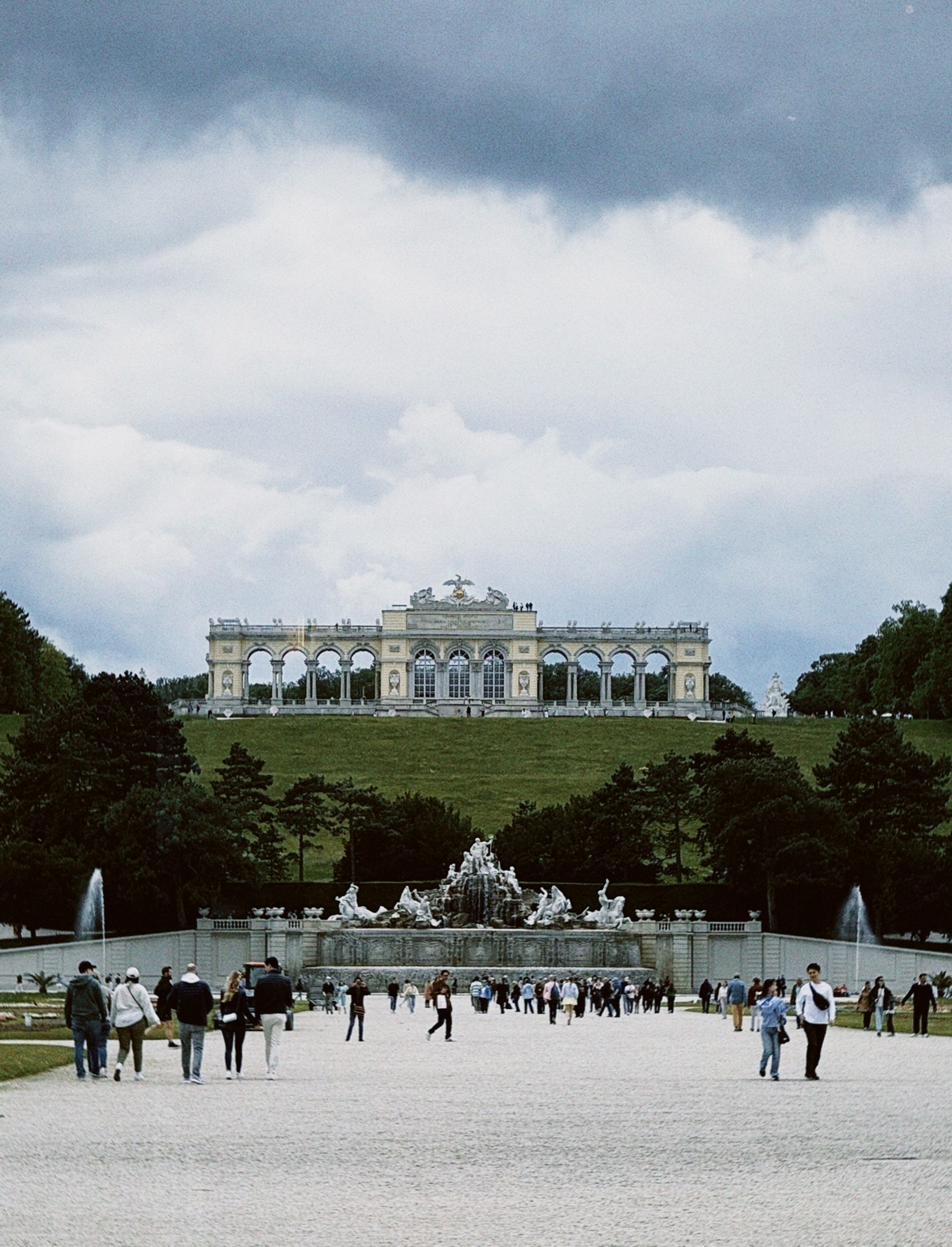 The Gloriette at Schönbrunn Palace in Vienna, Austria, viewed from the palace gardens with its central fountain and visitors in the foreground.