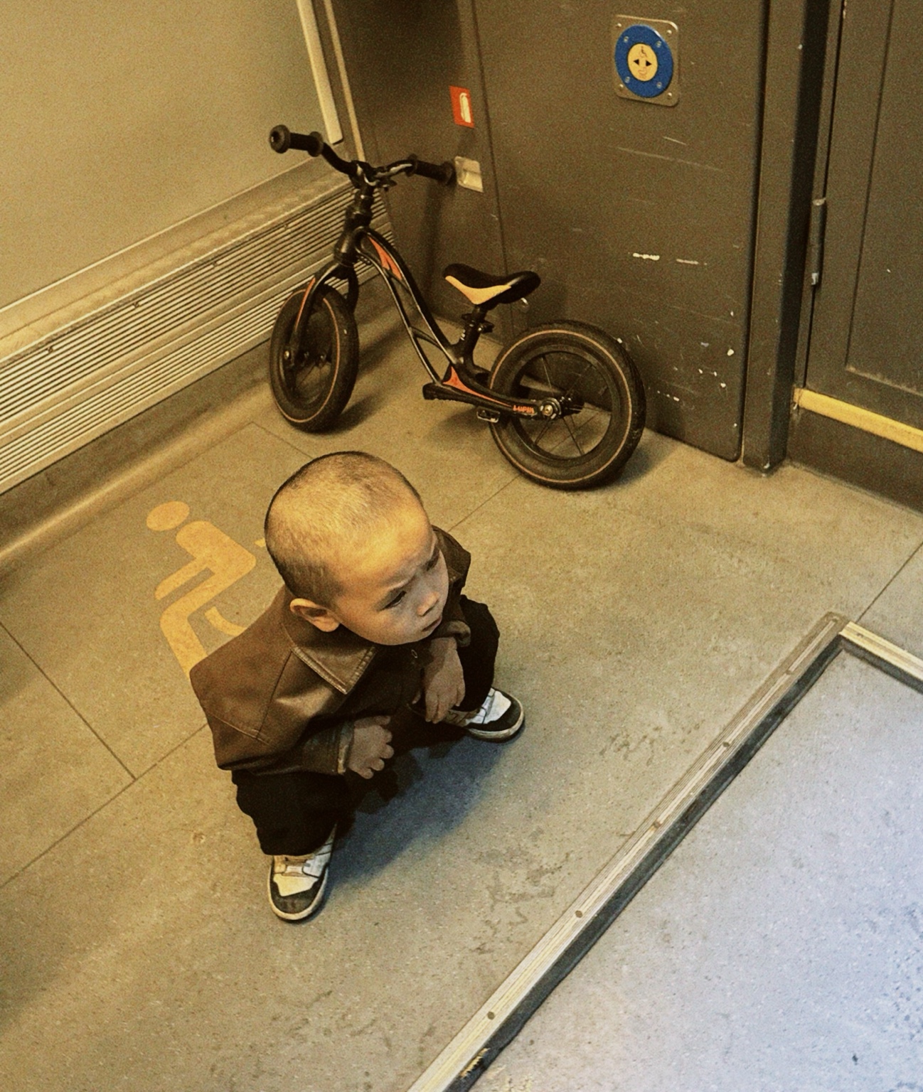 A child in fashionable dark clothing standing inside a Berlin tram beside a small bicycle, photographed in 2026.